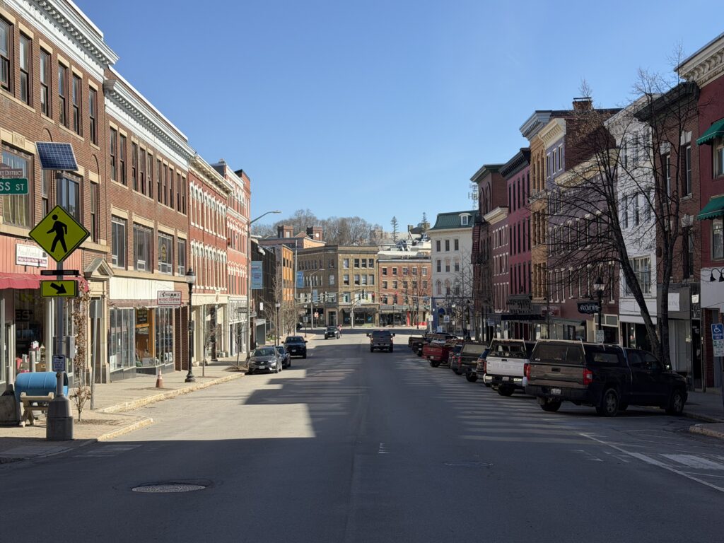 Historic brick storefronts line Main Street in downtown Bangor, Maine on a clear spring afternoon.
