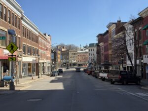 Historic brick storefronts line Main Street in downtown Bangor, Maine on a clear spring afternoon.