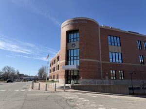 Penobscot Judicial Center, a three-story red brick courthouse with a rounded glass entrance tower and the Maine state seal, at 78 Exchange Street in downtown Bangor, Maine, under a clear blue sky