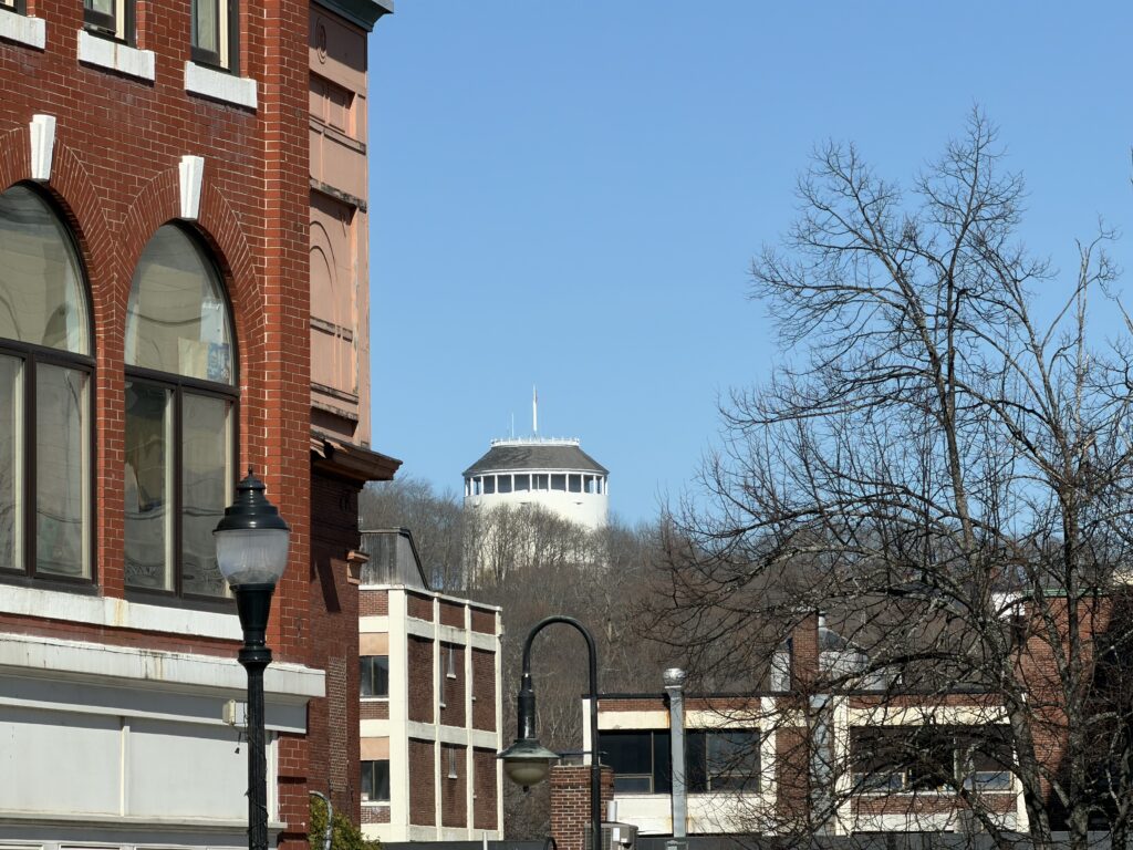 Thomas Hill Standpipe rising above downtown Bangor, Maine, framed by a historic red brick building and bare trees
