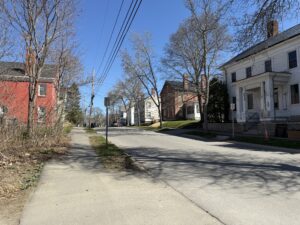 Quiet residential street in Bangor, Maine, lined with historic clapboard and brick homes on a clear spring day