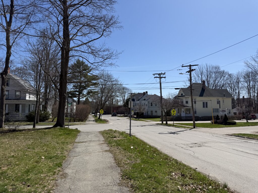Quiet residential street in Bangor, Maine with New England homes and tree-lined sidewalk in early spring
